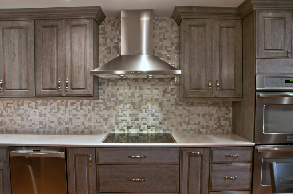 Example of a mid-sized transitional l-shaped medium tone wood floor eat-in kitchen design in Chicago with raised-panel cabinets, gray cabinets, quartz countertops, gray backsplash, mosaic tile backsplash, stainless steel appliances, an island and an undermount sink