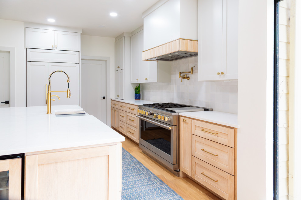 Mid-sized transitional l-shaped light wood floor open concept kitchen photo in Houston with light wood cabinets, white backsplash, porcelain backsplash, paneled appliances, an island and white countertops