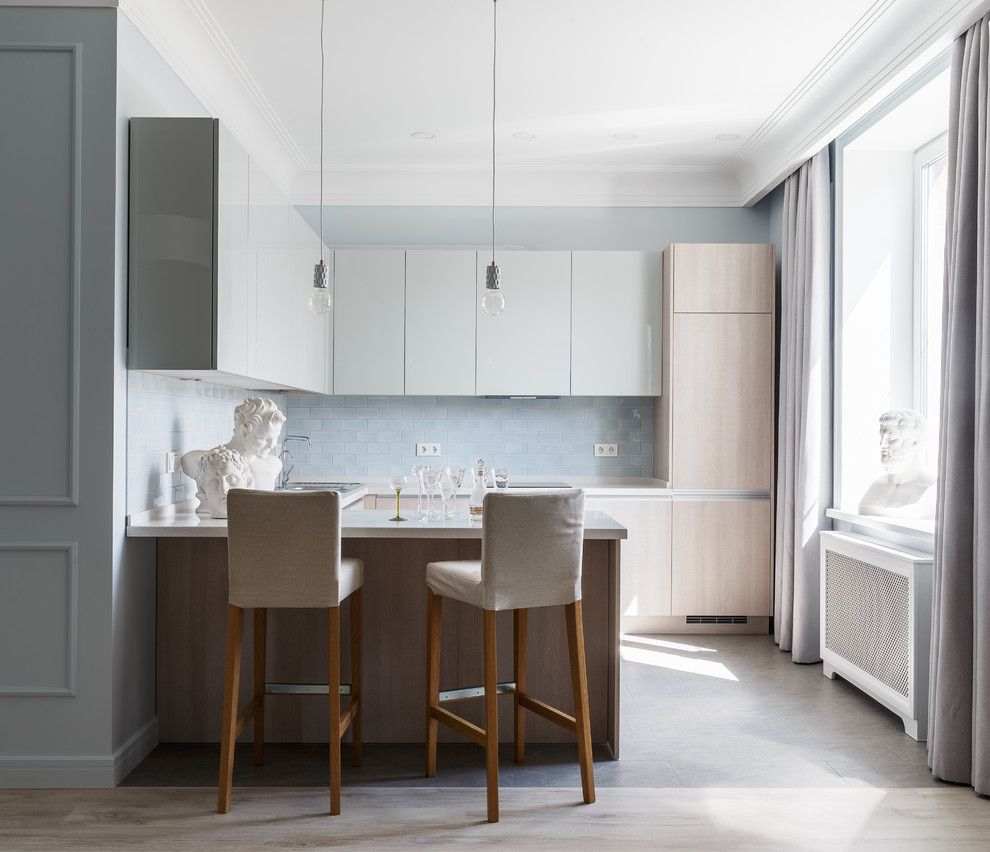 Photo of a classic u-shaped kitchen in Moscow with flat-panel cabinets, white worktops, light wood cabinets, blue splashback, metro tiled splashback, integrated appliances, a breakfast bar, grey floors, porcelain flooring and composite countertops.