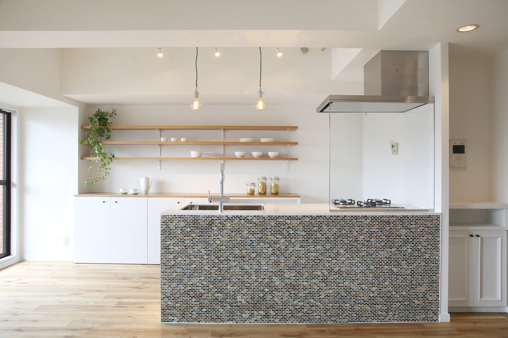 This is an example of a scandinavian galley kitchen in Other with a single-bowl sink, flat-panel cabinets, white cabinets, light hardwood floors and with island.