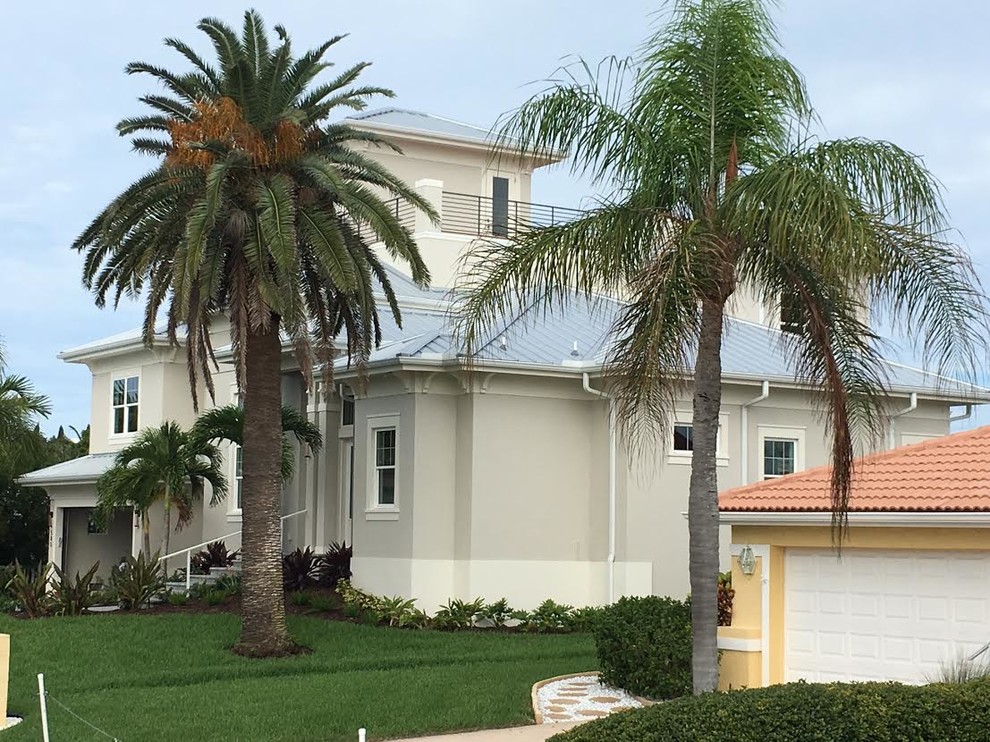 Large beach style two-storey stucco grey house exterior in Tampa with a hip roof and a metal roof.