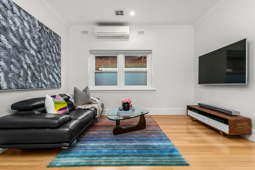 This is an example of a contemporary enclosed living room in Melbourne with white walls, light hardwood floors, a wall-mounted tv and beige floor.