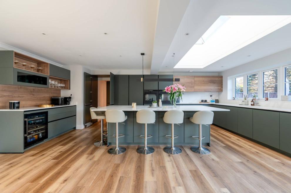 Design ideas for a large contemporary u-shaped kitchen/diner in Hertfordshire with a single-bowl sink, flat-panel cabinets, green cabinets, quartz worktops, black appliances, medium hardwood flooring, an island, brown floors and white worktops.