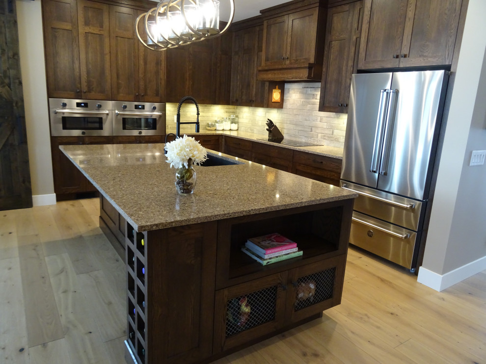 Large transitional l-shaped light wood floor and brown floor kitchen pantry photo with an undermount sink, shaker cabinets, medium tone wood cabinets, granite countertops, gray backsplash, stone tile backsplash, stainless steel appliances, an island and multicolored countertops