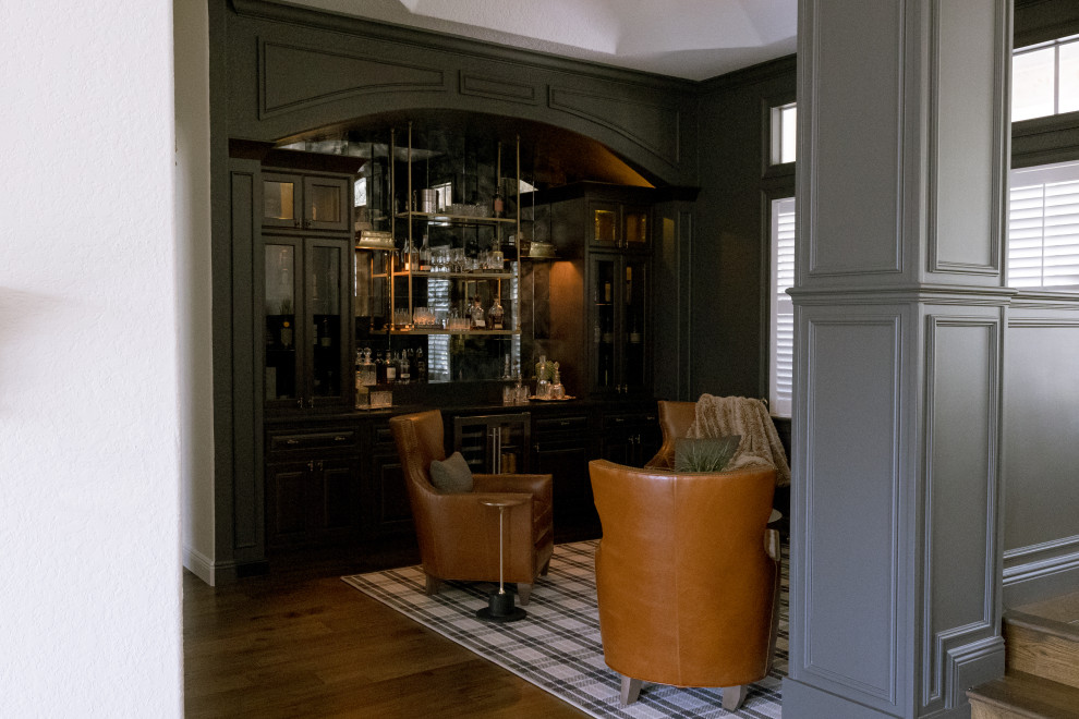 Inspiration for a mid-sized traditional wet bar in Orlando with glass-front cabinets, black cabinets, soapstone benchtops, mirror splashback, medium hardwood floors, brown floor and black benchtop.