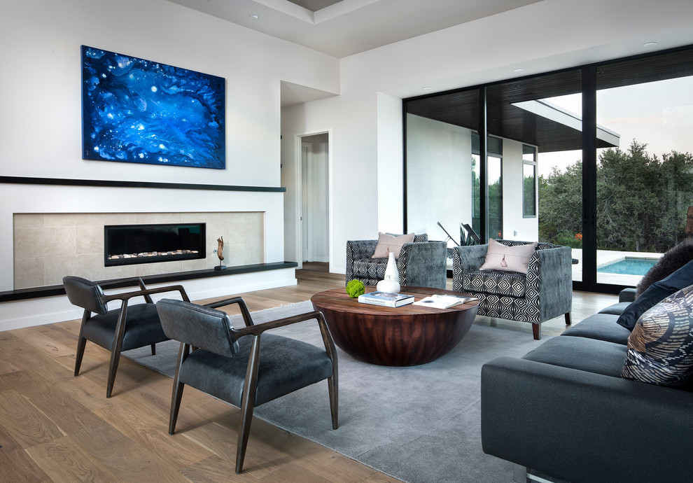 Photo of a large modern open concept living room in Austin with white walls, light hardwood floors, a ribbon fireplace, a tile fireplace surround and a concealed tv.