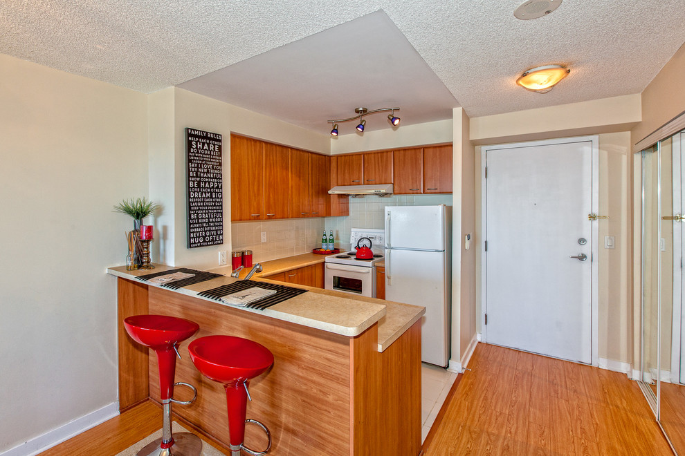 Example of a small transitional u-shaped ceramic tile eat-in kitchen design in Toronto with flat-panel cabinets, medium tone wood cabinets, solid surface countertops, white backsplash, subway tile backsplash, white appliances, a peninsula and a drop-in sink