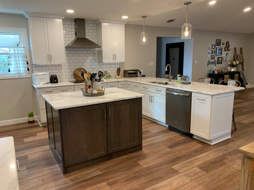 Example of a large transitional u-shaped vinyl floor and brown floor open concept kitchen design with an undermount sink, shaker cabinets, white cabinets, quartz countertops, white backsplash, ceramic backsplash, stainless steel appliances, an island and white countertops