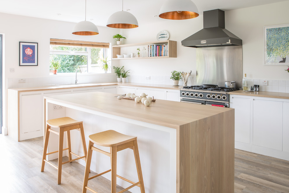 Photo of a large scandinavian l-shaped open plan kitchen in Other with a double-bowl sink, flat-panel cabinets, white cabinets, wood benchtops, white splashback, porcelain splashback, light hardwood floors and with island.