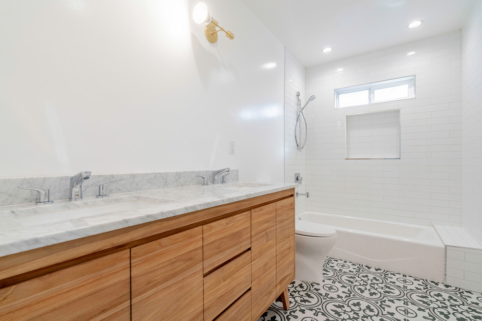 Mid-sized modern bathroom in Los Angeles with flat-panel cabinets, medium wood cabinets, an alcove tub, a shower/bathtub combo, a one-piece toilet, white tile, subway tile, white walls, ceramic floors, an undermount sink, marble benchtops, black floor, a shower curtain and white benchtops.