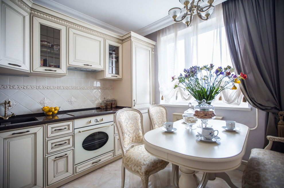 Design ideas for a traditional separate kitchen in Moscow with an undermount sink, raised-panel cabinets, beige cabinets, beige splashback, white appliances, beige floor and black benchtop.