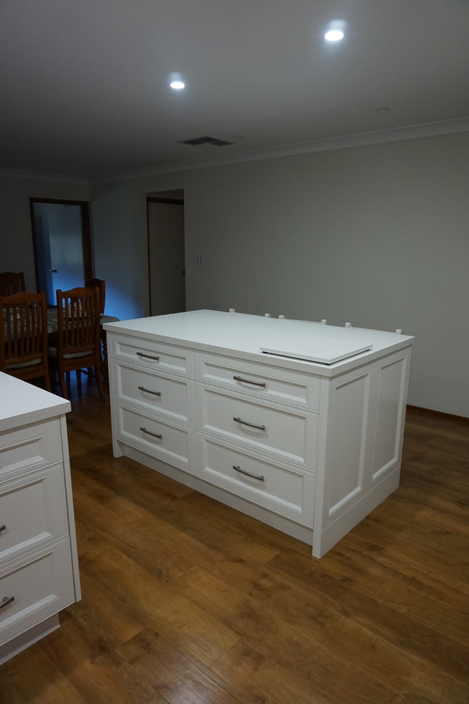 Photo of a large contemporary eat-in kitchen in Sydney with a drop-in sink, recessed-panel cabinets, white cabinets, quartz benchtops, white splashback, porcelain splashback, stainless steel appliances, light hardwood floors and with island.
