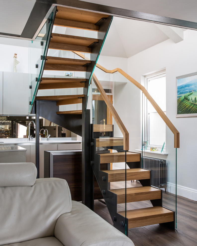 This is an example of a contemporary wood u-shaped staircase in West Midlands with open risers and glass railing.
