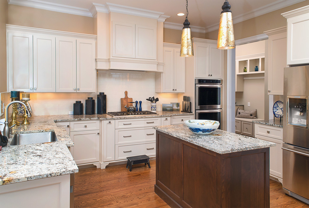 Photo of a mid-sized traditional u-shaped eat-in kitchen in Other with a single-bowl sink, recessed-panel cabinets, beige cabinets, granite benchtops, beige splashback, subway tile splashback, stainless steel appliances, medium hardwood floors, with island and brown floor.