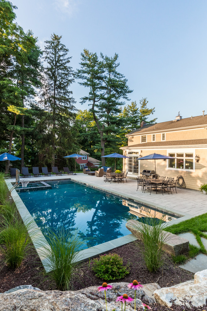 Large traditional backyard rectangular lap pool in New York with a hot tub and natural stone pavers.