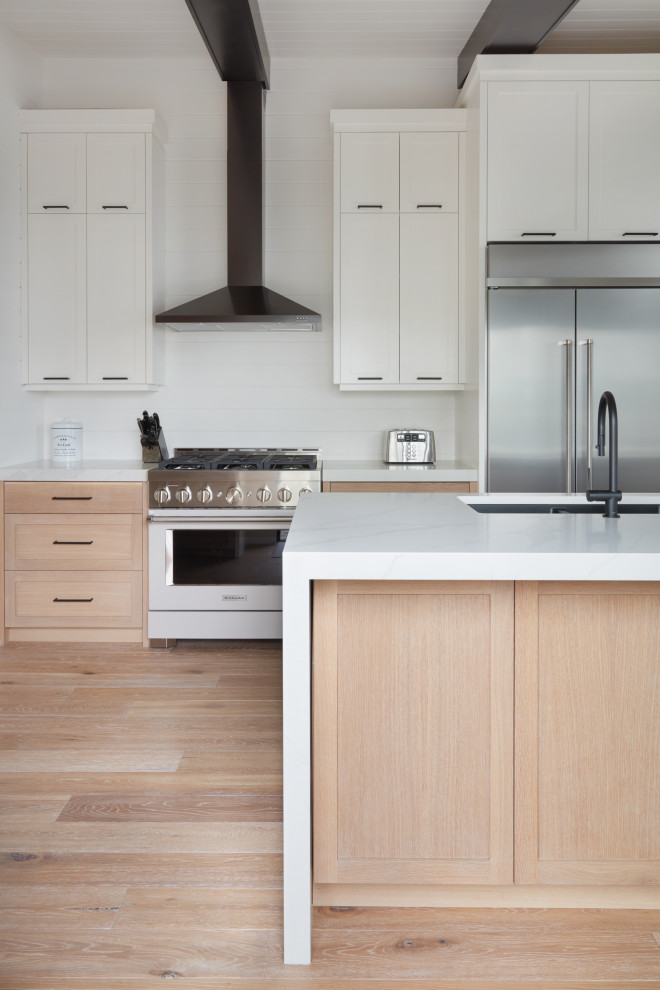 This is an example of a mid-sized contemporary l-shaped open plan kitchen in Toronto with an undermount sink, shaker cabinets, white cabinets, quartz benchtops, white splashback, shiplap splashback, stainless steel appliances, light hardwood floors, with island, beige floor, white benchtop and timber.