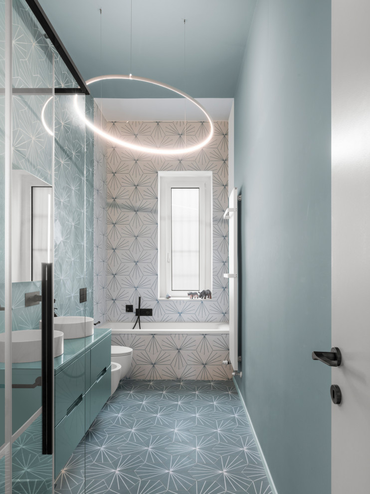 Стильный дизайн: узкая и длинная главная ванная комната среднего размера в современном стиле с плоскими фасадами, бирюзовыми фасадами, накладной ванной, угловым душем, инсталляцией, цементной плиткой, полом из цементной плитки, настольной раковиной, стеклянной столешницей, душем с раздвижными дверями, синей столешницей, тумбой под две раковины и подвесной тумбой - последний тренд