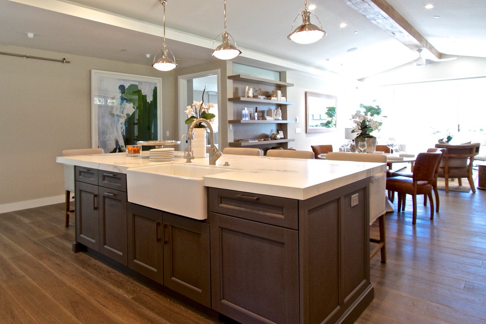 Large transitional single-wall dark wood floor eat-in kitchen photo in Orange County with a farmhouse sink, shaker cabinets, white cabinets, marble countertops, white backsplash, subway tile backsplash, stainless steel appliances and an island