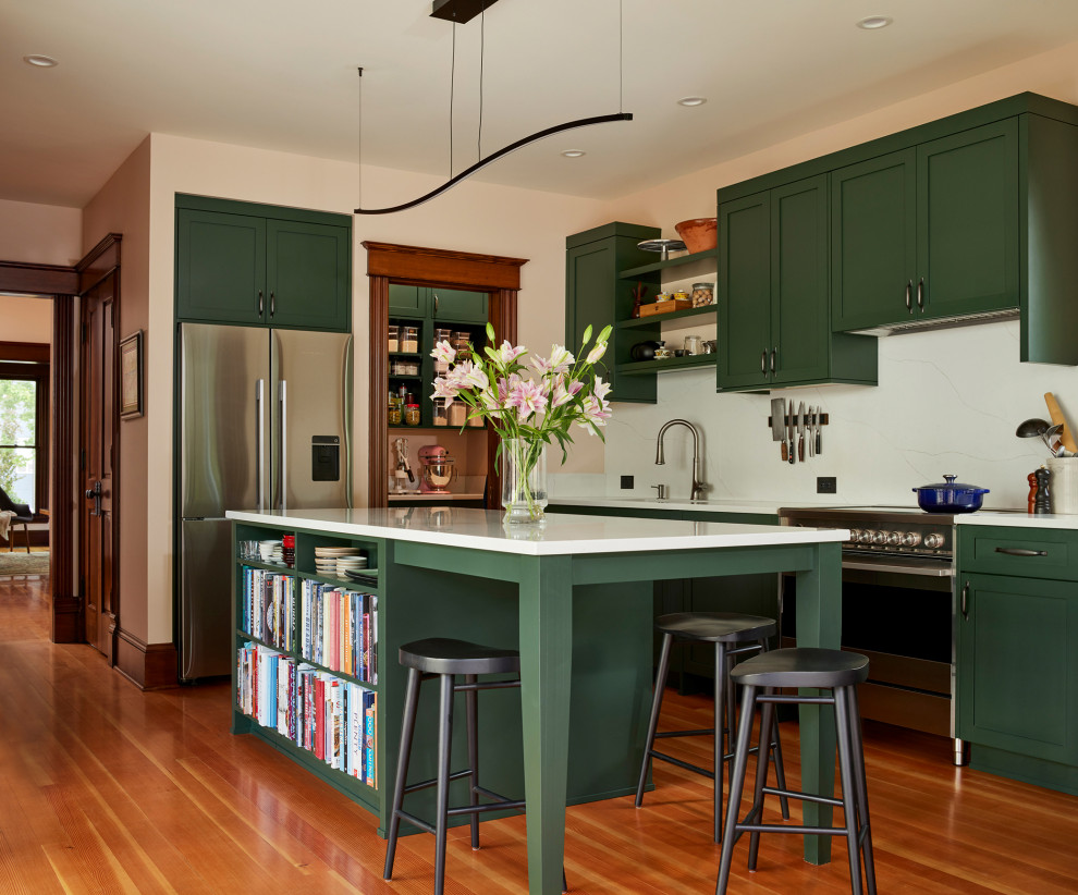 Mid-sized traditional eat-in kitchen in Seattle with an undermount sink, recessed-panel cabinets, green cabinets, quartz benchtops, engineered quartz splashback, stainless steel appliances, light hardwood floors, with island and white benchtop.