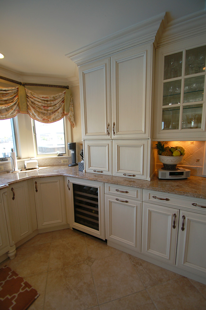 This is an example of a large traditional u-shaped eat-in kitchen in New York with an undermount sink, recessed-panel cabinets, white cabinets, granite benchtops, beige splashback, panelled appliances, limestone floors and with island.