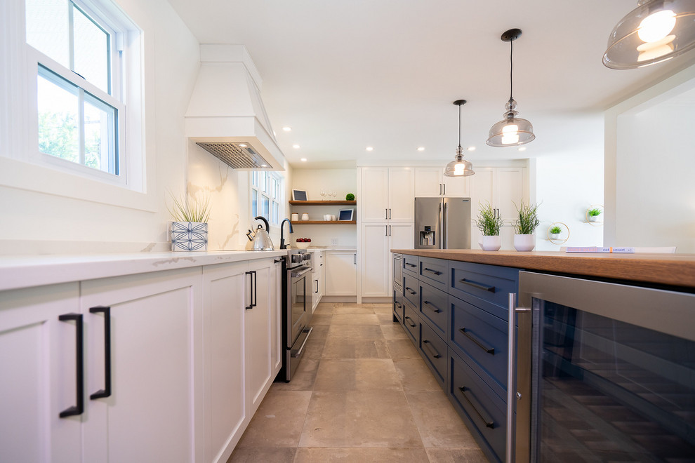 Photo of a large contemporary l-shaped eat-in kitchen in Montreal with a farmhouse sink, shaker cabinets, brown cabinets, wood benchtops, white splashback, porcelain splashback, stainless steel appliances, porcelain floors, with island, beige floor and white benchtop.