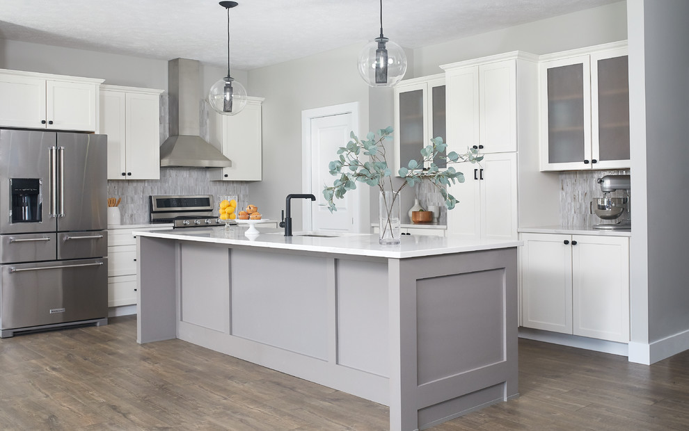 Design ideas for a mid-sized transitional kitchen with an undermount sink, shaker cabinets, white cabinets, quartz benchtops, grey splashback, stainless steel appliances, laminate floors, with island, brown floor and grey benchtop.