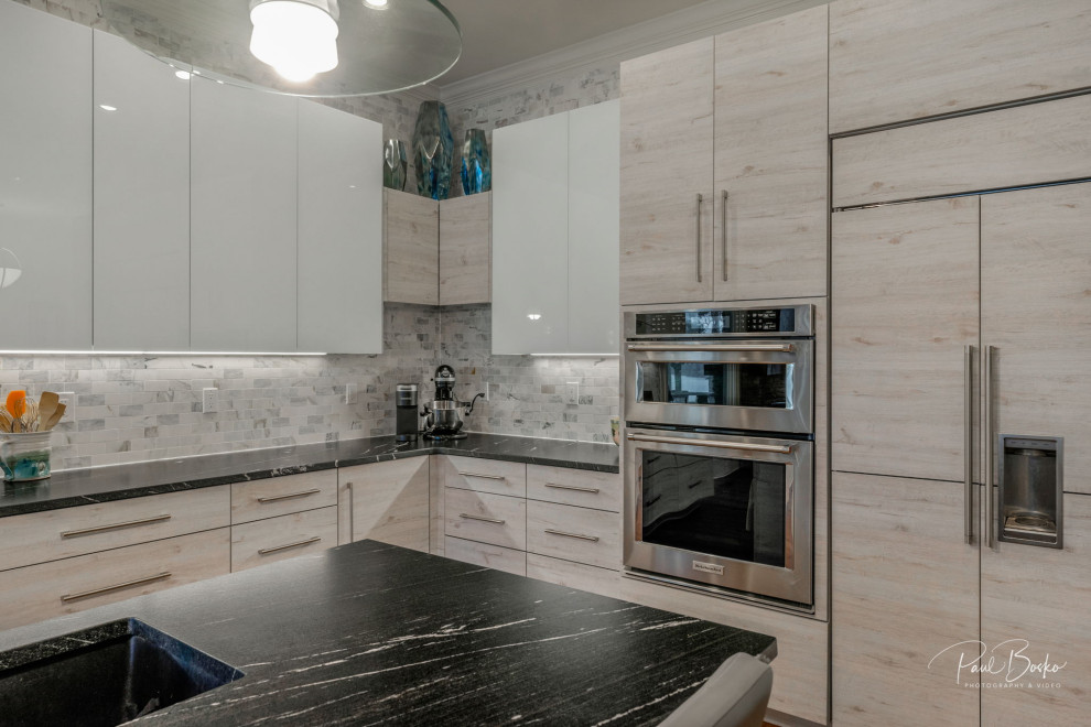 Inspiration for a modern l-shaped medium tone wood floor eat-in kitchen remodel in Charlotte with a single-bowl sink, flat-panel cabinets, distressed cabinets, granite countertops, multicolored backsplash, porcelain backsplash, stainless steel appliances, an island and black countertops