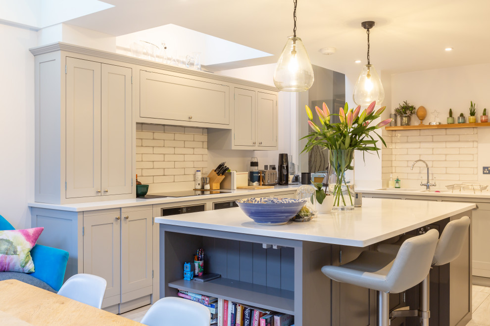 Transitional eat-in kitchen in London with shaker cabinets, grey cabinets, white splashback, stainless steel appliances, with island, grey floor and white benchtop.