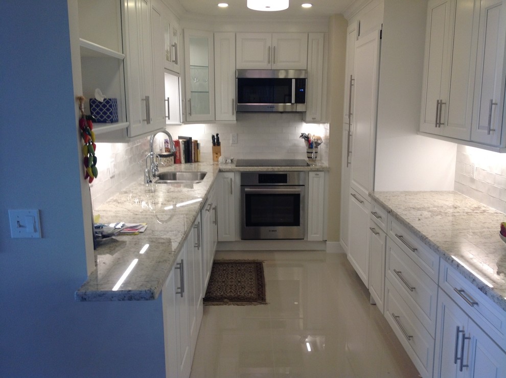 Photo of a contemporary galley separate kitchen in Miami with raised-panel cabinets, white cabinets, granite benchtops, white splashback, subway tile splashback, panelled appliances, an undermount sink, ceramic floors and no island.