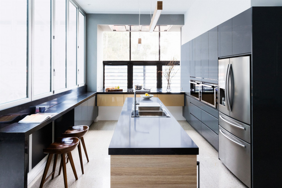 This is an example of a large u-shaped eat-in kitchen in Melbourne with a drop-in sink, flat-panel cabinets, black cabinets, stainless steel appliances and with island.
