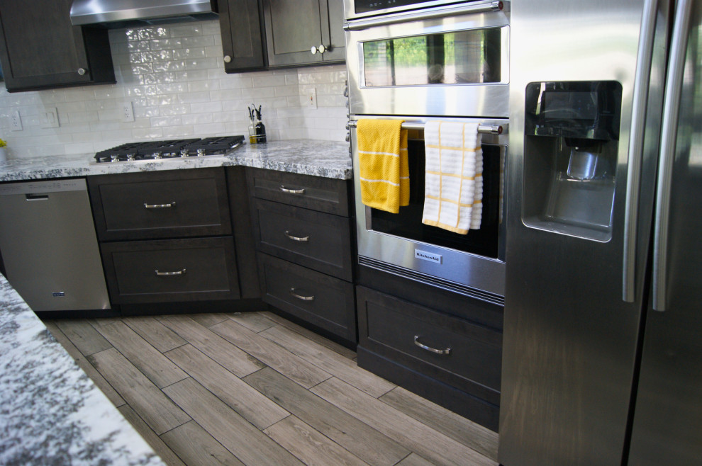 Example of a mid-sized minimalist l-shaped porcelain tile and gray floor open concept kitchen design in Phoenix with an undermount sink, shaker cabinets, brown cabinets, granite countertops, white backsplash, subway tile backsplash, stainless steel appliances, an island and white countertops
