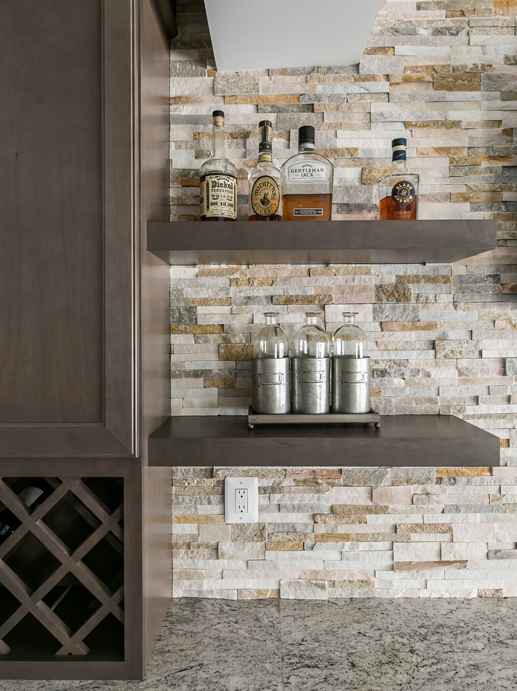 Design ideas for a large transitional single-wall seated home bar in DC Metro with recessed-panel cabinets, brown cabinets, granite benchtops, beige splashback, stone tile splashback, laminate floors, brown floor, an undermount sink and grey benchtop.