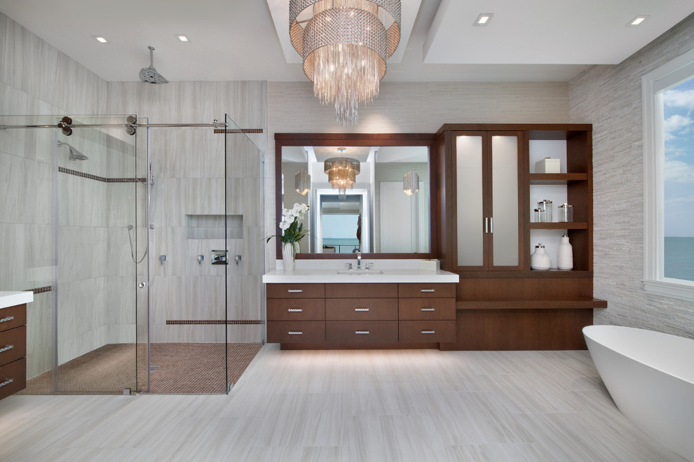 Large contemporary master bathroom in Miami with flat-panel cabinets, medium wood cabinets, a freestanding tub, a corner shower, gray tile, stone tile, grey walls, porcelain floors, an undermount sink, engineered quartz benchtops, beige floor, a sliding shower screen and white benchtops.