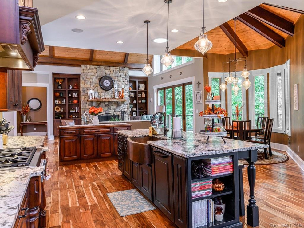 Open concept kitchen - rustic medium tone wood floor open concept kitchen idea with a farmhouse sink, dark wood cabinets, granite countertops, beige backsplash, an island and white countertops