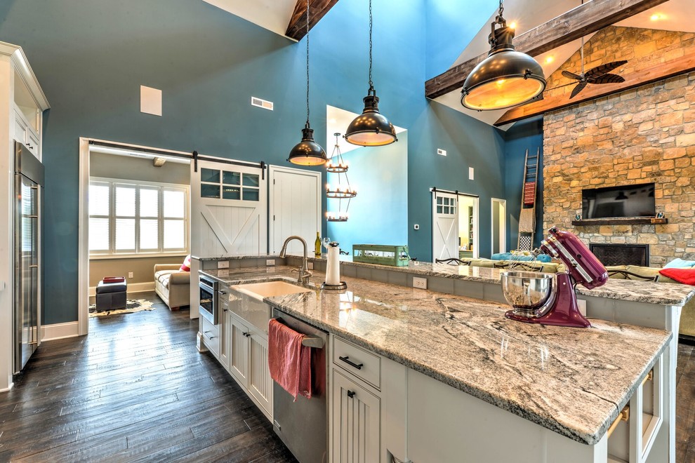This is an example of an expansive beach style l-shaped open plan kitchen in Other with a farmhouse sink, louvered cabinets, white cabinets, granite benchtops, beige splashback, subway tile splashback, stainless steel appliances, dark hardwood floors, with island and brown floor.