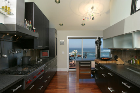 Enclosed kitchen - mid-sized modern galley light wood floor and beige floor enclosed kitchen idea with flat-panel cabinets, black cabinets, granite countertops, beige backsplash, porcelain backsplash, stainless steel appliances and no island