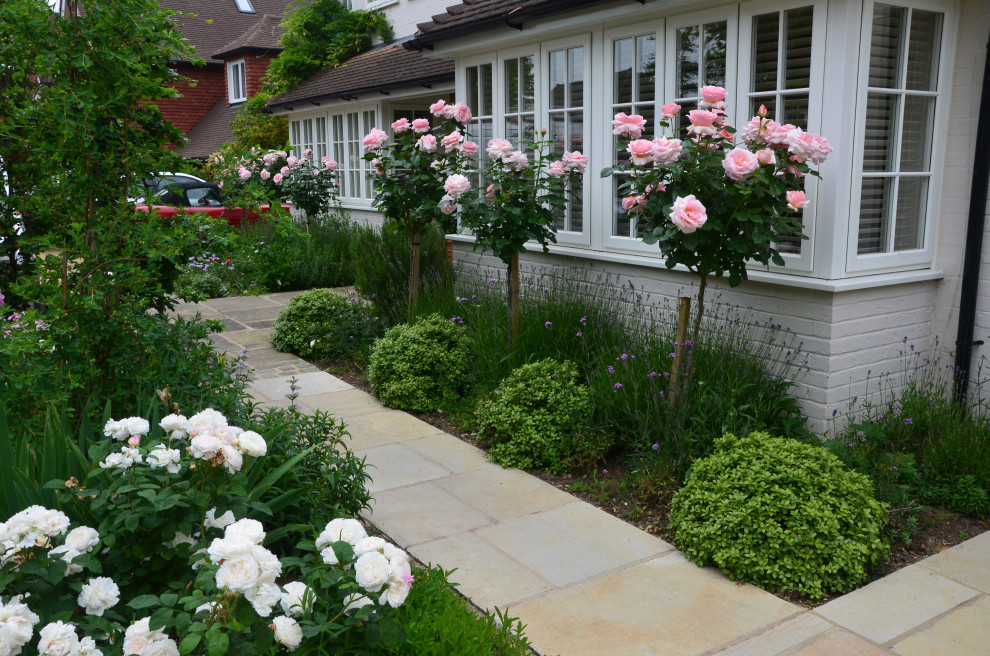 This is an example of a traditional front yard full sun formal garden for summer in Surrey with with flowerbed, natural stone pavers and a wood fence.