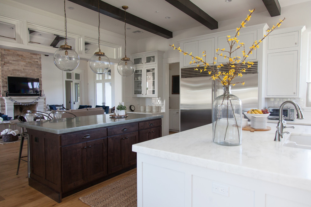 Inspiration for a large transitional l-shaped light wood floor eat-in kitchen remodel in Phoenix with a farmhouse sink, white backsplash, stainless steel appliances, an island, stainless steel countertops, shaker cabinets, white cabinets and porcelain backsplash