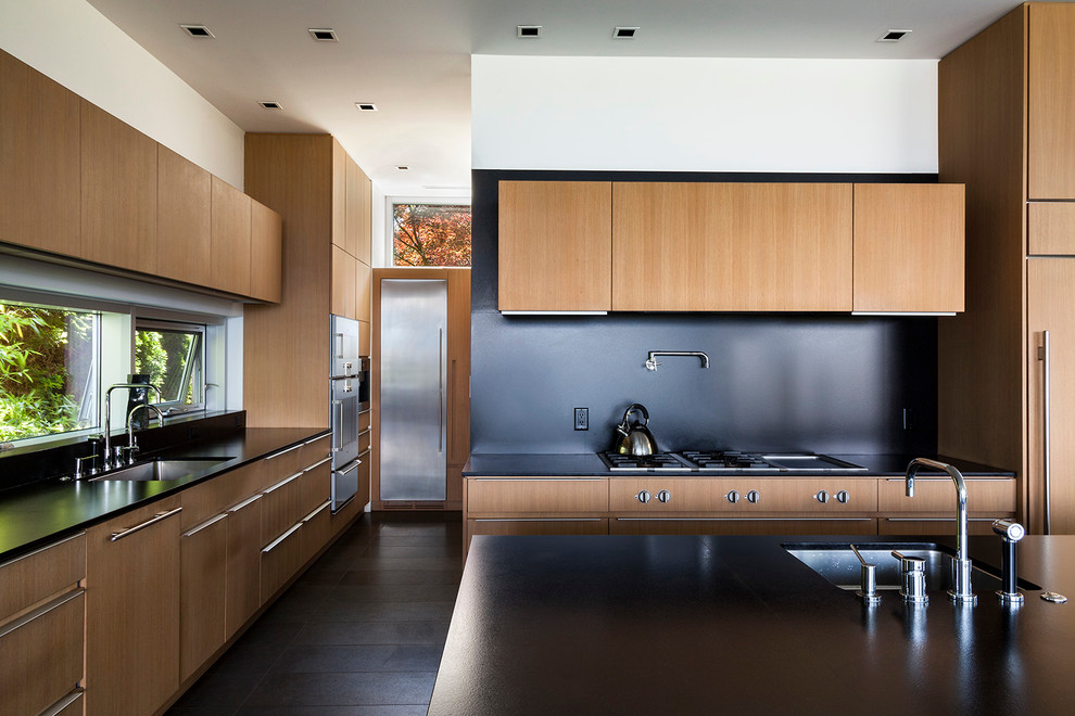 Mid-sized contemporary l-shaped open plan kitchen in Vancouver with an undermount sink, flat-panel cabinets, medium wood cabinets, black splashback, dark hardwood floors, with island, solid surface benchtops, stone slab splashback, stainless steel appliances and brown floor.