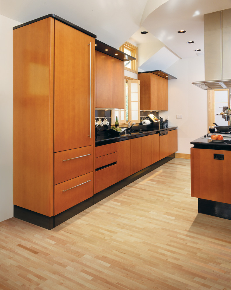 Mid-sized modern galley open plan kitchen in Detroit with flat-panel cabinets, medium wood cabinets, solid surface benchtops, black splashback, porcelain splashback and light hardwood floors.