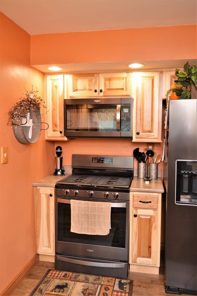 Photo of a mid-sized country u-shaped eat-in kitchen in Other with an undermount sink, raised-panel cabinets, light wood cabinets, solid surface benchtops, stainless steel appliances, laminate floors, a peninsula, brown floor and brown benchtop.