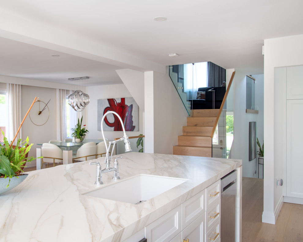 Example of a mid-sized transitional galley light wood floor and beige floor open concept kitchen design in Ottawa with an undermount sink, recessed-panel cabinets, white cabinets, quartz countertops, white backsplash, porcelain backsplash, stainless steel appliances, an island and white countertops