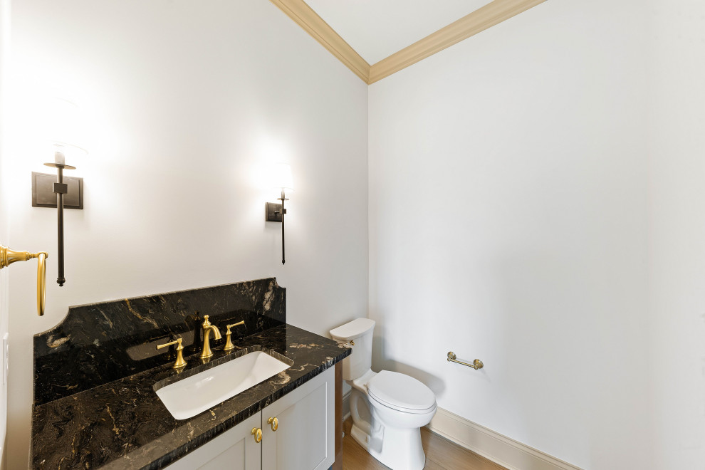 Cette photo montre un grand WC et toilettes chic avec un placard à porte shaker, des portes de placard blanches, WC à poser, un mur blanc, un sol en vinyl, un lavabo encastré, un plan de toilette en quartz, un sol gris, un plan de toilette noir et meuble-lavabo encastré.
