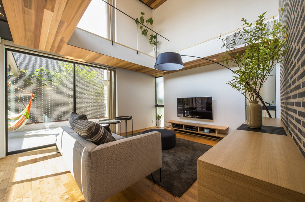 Diseño de salón abierto minimalista con paredes blancas, suelo de madera en tonos medios, televisor colgado en la pared y suelo marrón