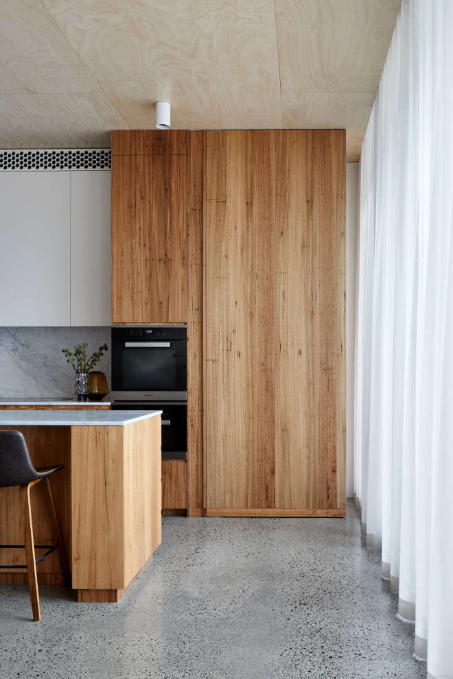 Large contemporary l-shaped eat-in kitchen in Melbourne with a double-bowl sink, flat-panel cabinets, medium wood cabinets, marble benchtops, white splashback, marble splashback, stainless steel appliances, terrazzo floors, with island, grey floor and white benchtop.