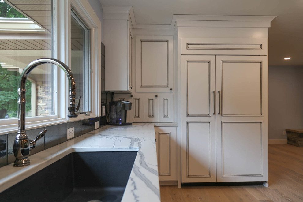 Mid-sized transitional u-shaped light wood floor and beige floor eat-in kitchen photo with an undermount sink, recessed-panel cabinets, white cabinets, quartzite countertops, black backsplash, porcelain backsplash, stainless steel appliances, an island and white countertops