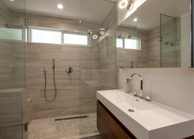 Photo of a midcentury master bathroom in Other with an integrated sink, furniture-like cabinets, medium wood cabinets, onyx benchtops, an open shower, gray tile, porcelain tile, white walls and concrete floors.