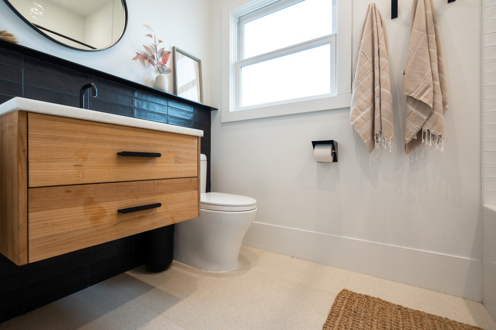 Photo of a small traditional bathroom in San Francisco with flat-panel cabinets, light wood cabinets, an alcove bath, a shower/bath combination, a two-piece toilet, black and white tiles, porcelain tiles, white walls, ceramic flooring, a submerged sink, engineered stone worktops, beige floors, a shower curtain, white worktops, a wall niche, a single sink and a floating vanity unit.