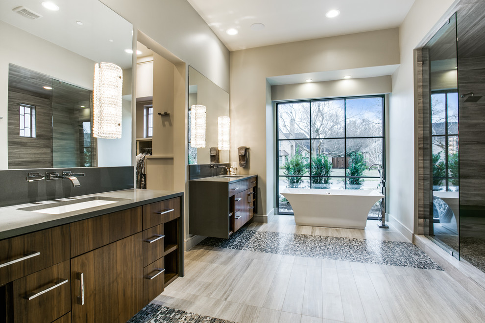 Design ideas for a mid-sized contemporary master bathroom in Dallas with flat-panel cabinets, brown cabinets, a freestanding tub, a double shower, a two-piece toilet, gray tile, glass sheet wall, beige walls, ceramic floors, an undermount sink, limestone benchtops, grey floor and a hinged shower door.