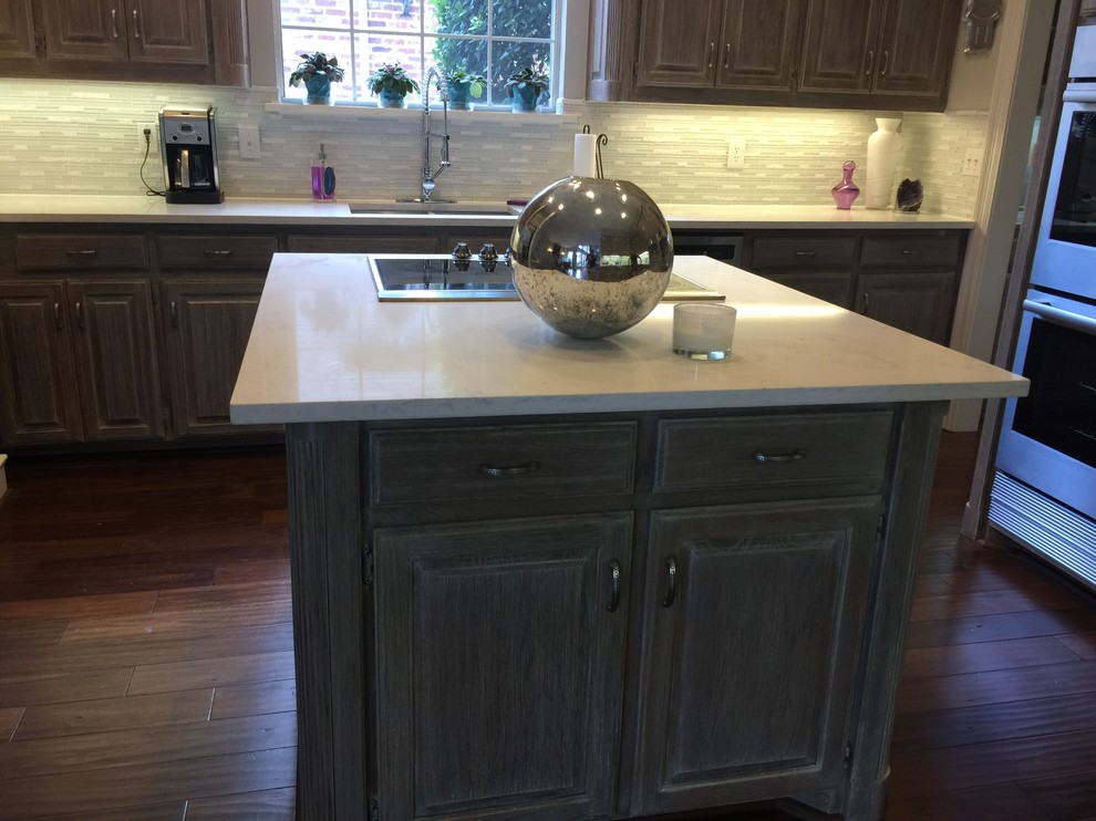 Inspiration for a mid-sized transitional l-shaped dark wood floor and brown floor enclosed kitchen remodel in Dallas with an undermount sink, raised-panel cabinets, dark wood cabinets, quartz countertops, white backsplash, matchstick tile backsplash, stainless steel appliances and an island